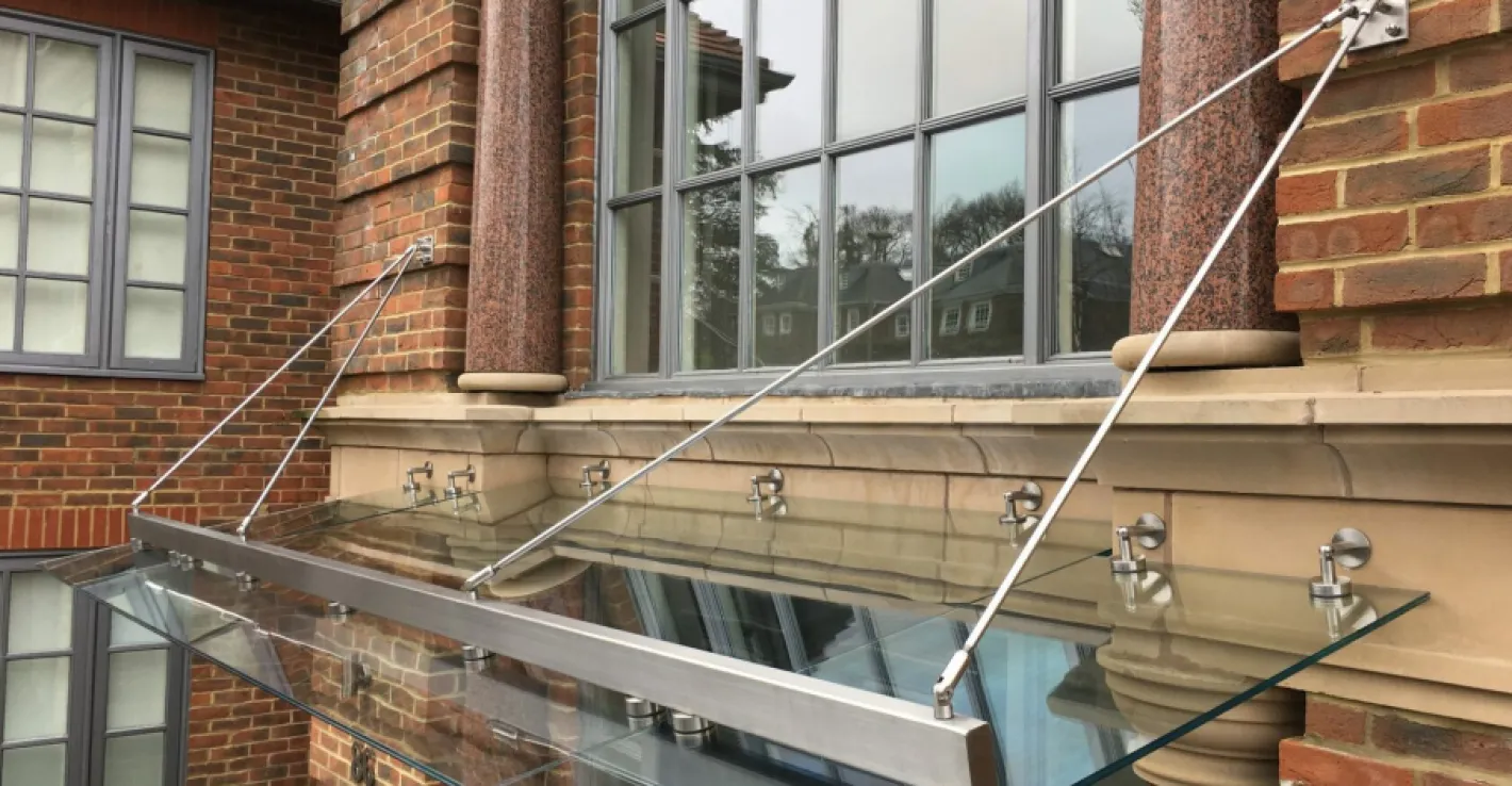 Стеклянный козырёк украшает фасад загородного дома и защищает вход от осадков.